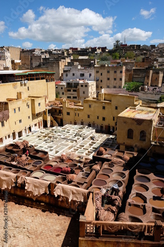 Leather tanning dye house in Fez, Morocco. Blue sunny sky white cloud.  brown yellow white dye vats surround by native residential houses photo