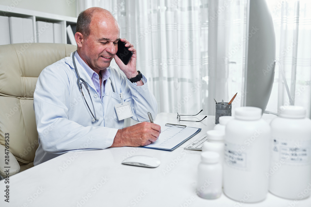 Smiling cardiologist checking cardiogram and consulting patient on the phone