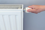 Hand adjusting thermostat valve of heating radiator in a room.