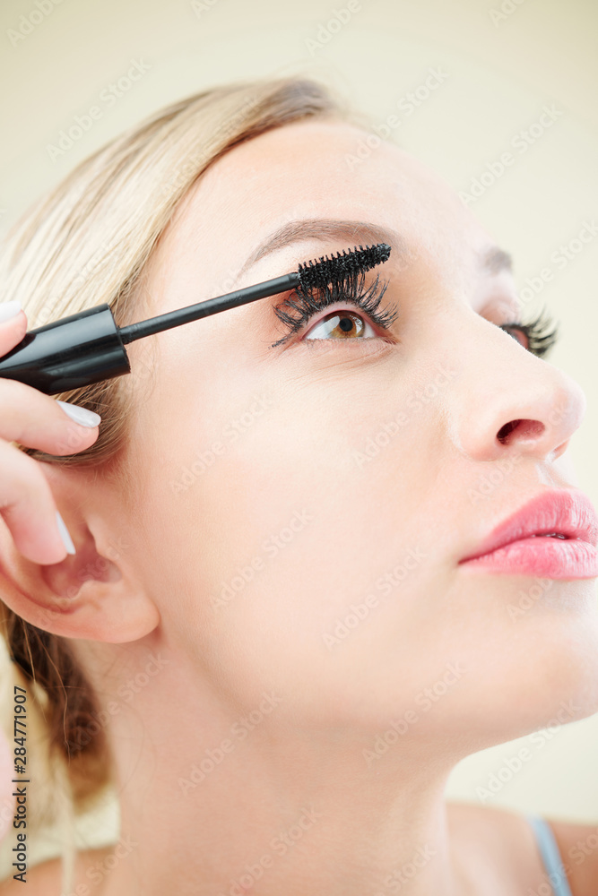 Close-up image of pretty young woman applying second coat of black mascara on her eyelashes