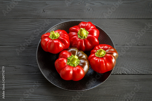 Four red bell peppers on a black plate on a dark wooden old background.