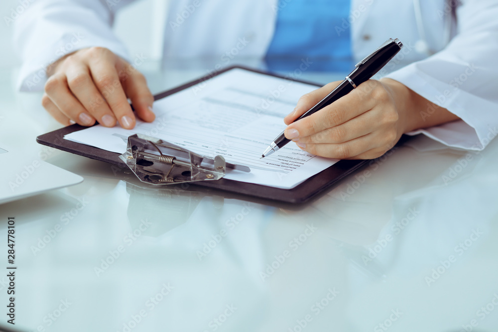 Fototapeta premium Doctor woman filling up medical form while sitting at the table, close-up of hands