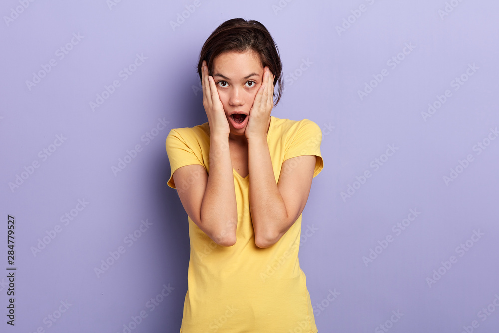 emotional girl touching her cheeks, expresses amazement, has mouth wide opened, can not believe in shocking news, isolated over blue. lifestyle, facial expression emotional girl touching her cheeks, expresses amazement, has mouth wide opened, can not believe in shocking news, isolated over blue. lifestyle, facial expression
