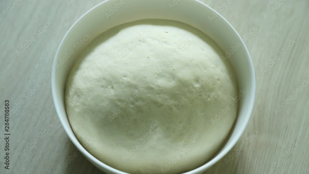 Dough rising, time lapse. Yeast dough rising on white bowl on wooden table. Pizza dough, khachapuri dough Dough rising, time lapse. Yeast dough rising on white bowl on wooden table. Pizza dough, khachapuri dough