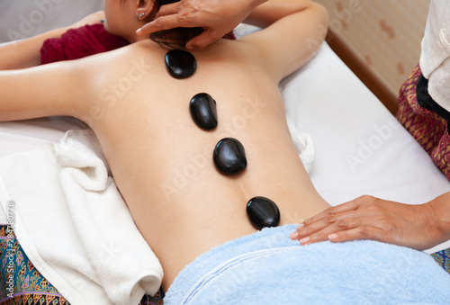 beautiful young woman lying on bed  spa and on her back is  hot stone for treatment healthy.