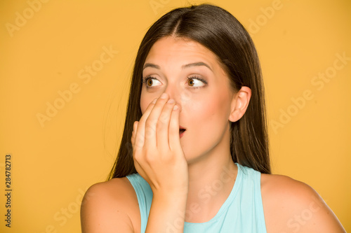 Portrait of beautiful young woman checking her breath on yellow background