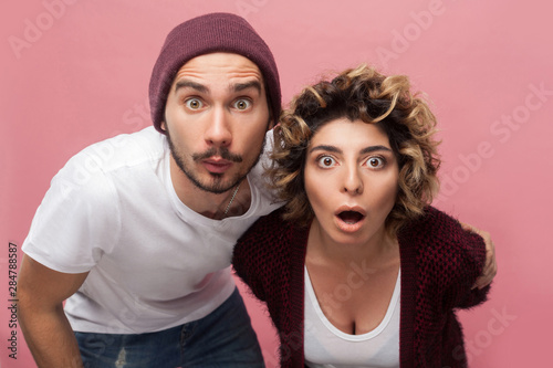 Closeup portrait of shocked funny couple of friends in casual style standing with unbeliveable face and looking at camera with big eyes and opened mouth. Isolated,indoor, studio shot, pink background photo