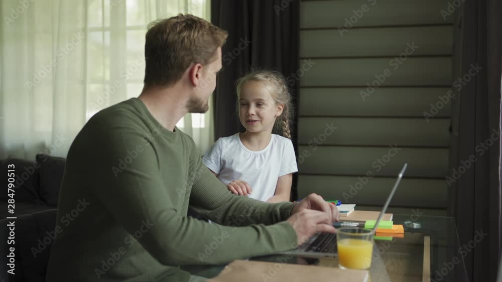 Tracking right shot of cute little daughter coming to loving father sitting at desk and working on laptop at home. Father and daughter talking and embracing warmly Tracking right shot of cute little daughter coming to loving father sitting at desk and working on laptop at home. Father and daughter talking and embracing warmly