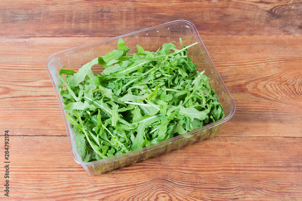 Fresh arugula leaves in container on rustic table, top view Fresh arugula leaves in container on rustic table, top view