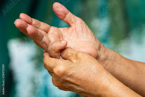 Trigger Finger, Senior woman's left hand massaging her little finger, Suffering from pain, Close up and macro shot, Swimming pool background, Health care concept