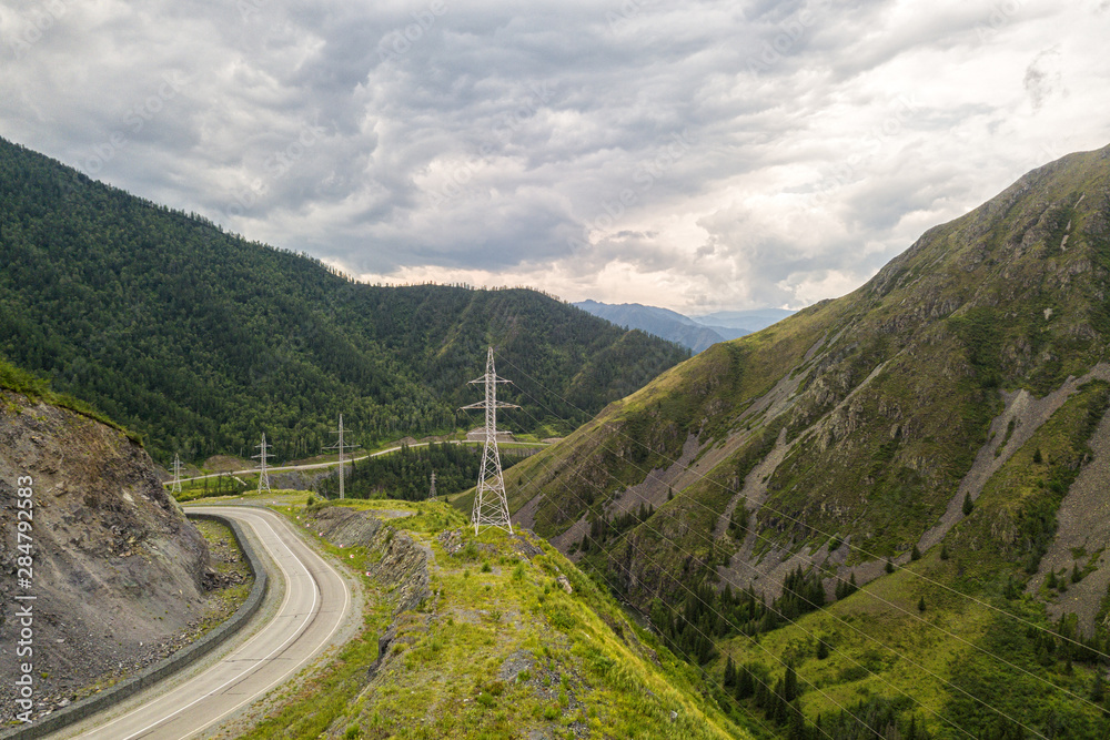 Asphalt road with huge power transmission towers. Landscape with beautiful mountain road with a perfect asphalt. High rocks, amazing sky at sunset in summer. Travel background. Highway at mountains Asphalt road with huge power transmission towers. Landscape with beautiful mountain road with a perfect asphalt. High rocks, amazing sky at sunset in summer. Travel background. Highway at mountains