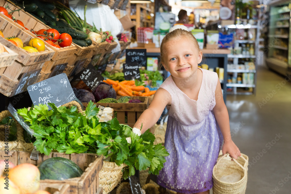 girl choosing parsley in vegetable shop. on the signboard inscriptions in Catalan