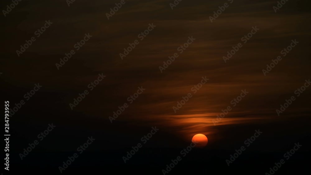 Timelapse of the setting sun behind the clouds at sunset over the small town. Swirling clouds before sunset. Low key Timelapse of the setting sun behind the clouds at sunset over the small town. Swirling clouds before sunset. Low key