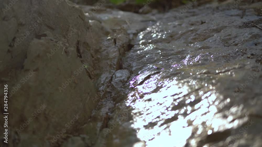A thin stream of water flows down descending rock formation, close up A thin stream of water flows down descending rock formation, close up