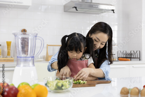 Happy Asian family Mother and child daughter are preparing the salad and cutting vegetables. cooking food in kitchen at home. Healthy food concept