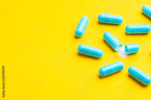 Blue tablets in capsules. One capsule is open. Yellow background. Copy space for text.