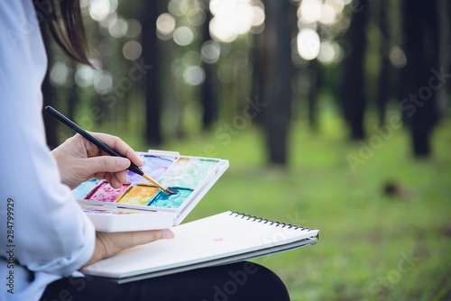 Relax woman painting water colour art work in green garden forest nature - people with creative art in nature stress reduction and meditation concept