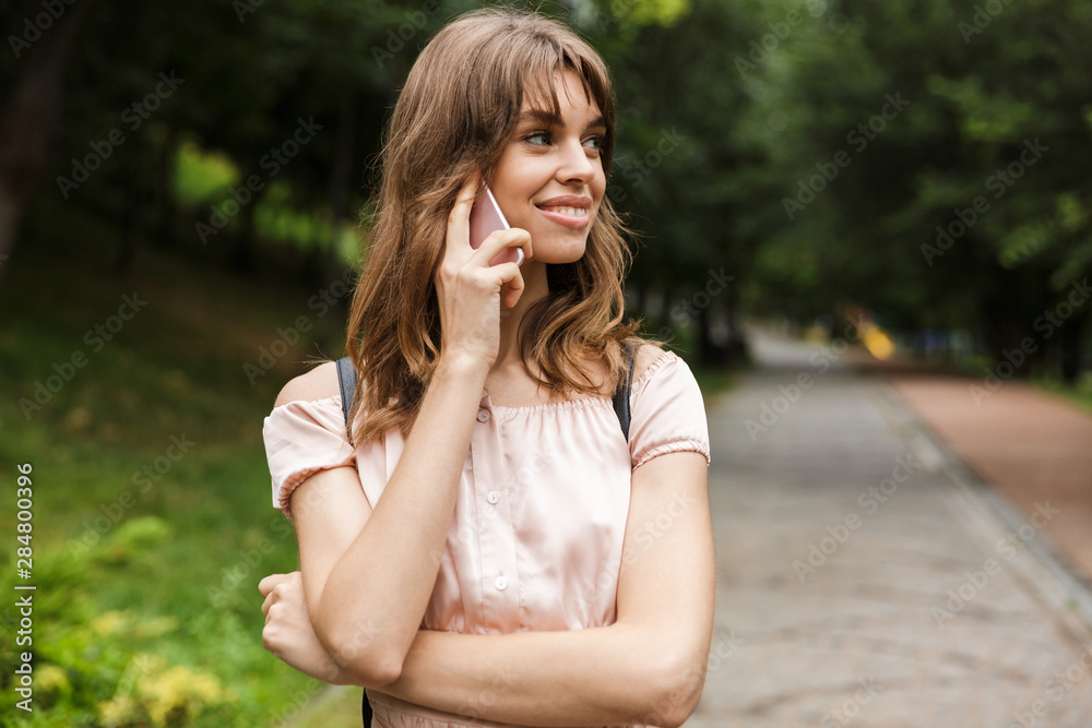 Portrait of happy smiling woman talking on cellphone while walking in summer park Portrait of happy smiling woman talking on cellphone while walking in summer park
