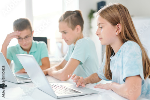 Young serious schoolgirl and her classmates working individually