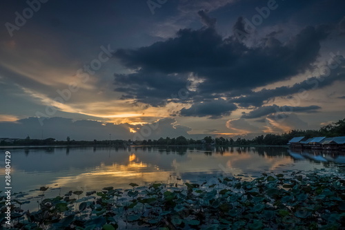 Fototapeta Naklejka Na Ścianę i Meble -  Lake view evening above Lotus lake with cloudy and yellow sun light in the sky background, sunset at Krajub Lake attraction in Ban Pong, Ratchaburi, Thailand.