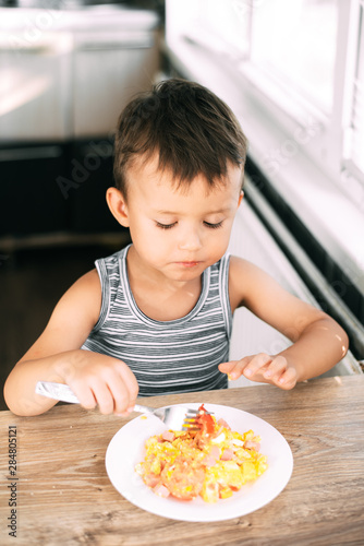a child in a t-shirt in the kitchen eating an omelet with sausage and tomatoes