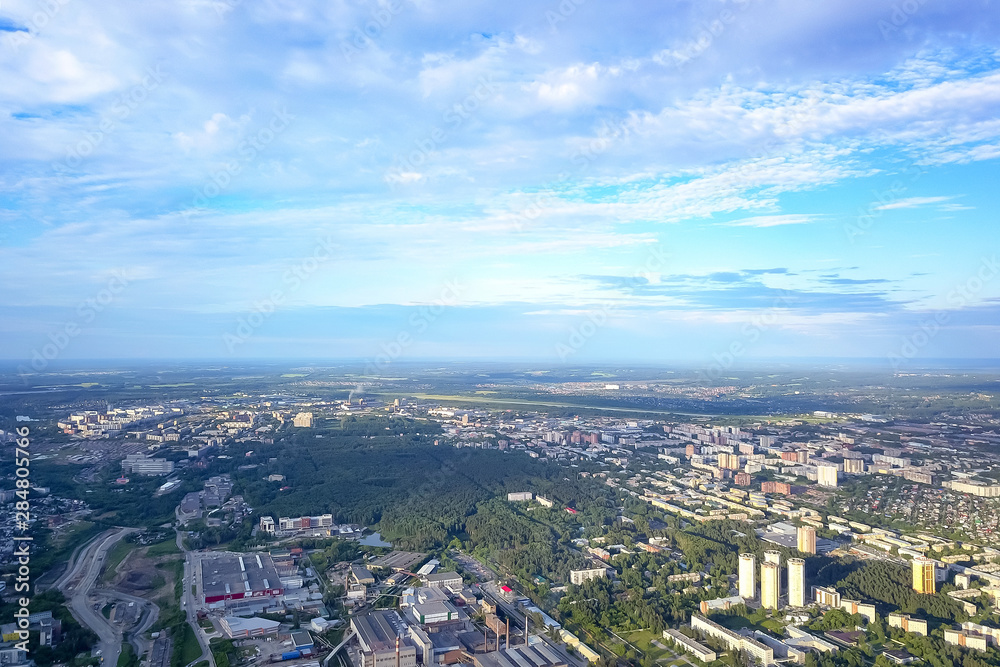 Aerial view of the cityscape with a lot of houses and buildings on a summer clear day under a blue sky with gray clouds in Novosibirsk.