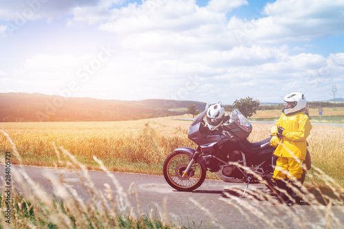 The driver girl in helmet is wearing a raincoat. Adventure motorbike with bags. a motorcycle tour journey. Outdoor. light warm tinting, glow, freedom concept. field and sky on background, copy space