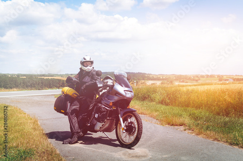 A male driver in a raincoat is standing by adventure motorbike with side bags. a motorcycle tour journey. Outdoor. World travel on two wheels, freedom concept. rider equipment.