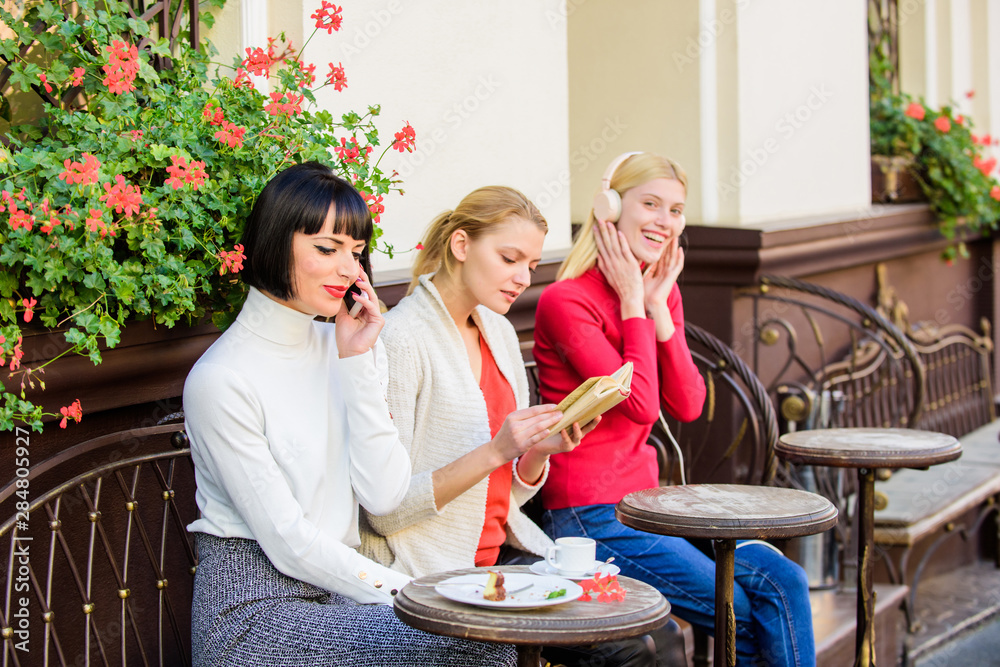 Obraz premium Group pretty women cafe terrace entertain themselves with reading speaking and listening. Information source. Female leisure. Weekend relax and leisure. Different interests. Hobby and leisure