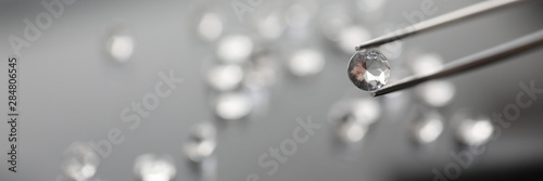 The jeweler holds a diamond in tweezers on a gray background. Selling gems concept.