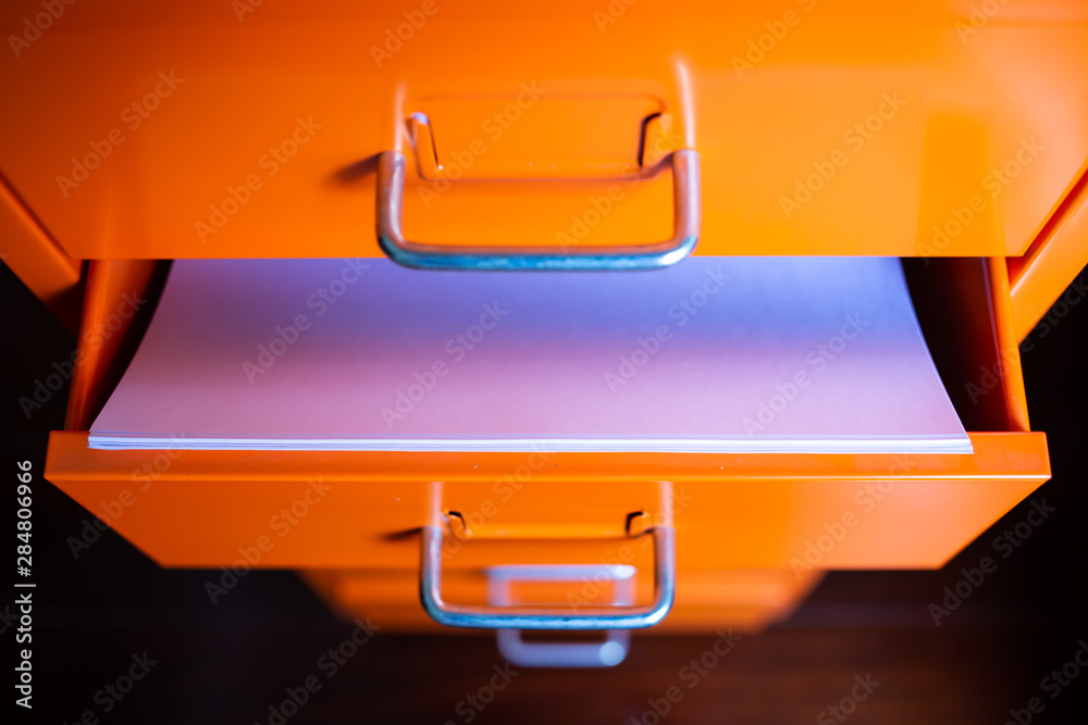 Filing cabinet with open drawer, White papers for write letter, Orange metal colour, Administration and storage, Close up shot, Selective focus, Stationery, Business concept Filing cabinet with open drawer, White papers for write letter, Orange metal colour, Administration and storage, Close up shot, Selective focus, Stationery, Business concept