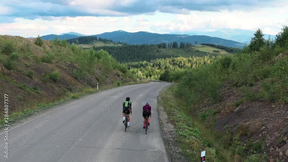 Aerial shot of man and woman cycling on the asphalt road in mountains. Travel by bicycle. Outdoor activities concept Aerial shot of man and woman cycling on the asphalt road in mountains. Travel by bicycle. Outdoor activities concept