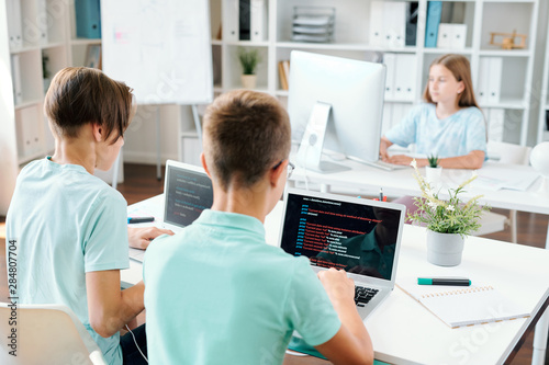 Two boys by laptops and schoolgirl working over school project individually