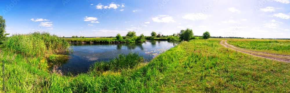 Meadow with river and country road under blue sky