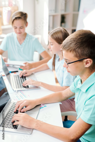 Two boys and girl sitting in front of laptops while carrying out final exam test