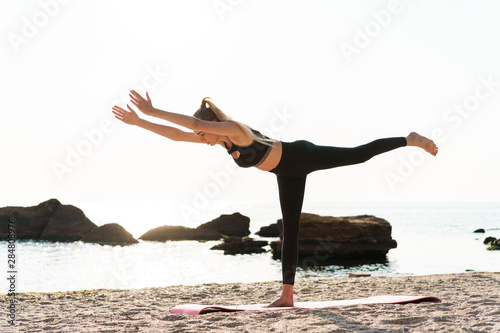 Image of calm athletic woman doing yoga exercises at seaside in morning