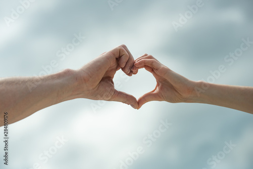 Heart sign. Hands show a heart symbol on sky background. Love. Man and woman. Partnership. Gender Equality. Love between man and woman. © Tverdokhlib