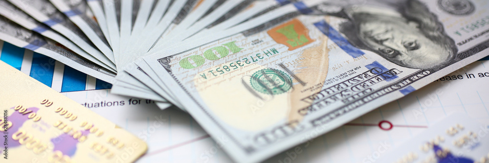 Big amount of US currency on financial statistics graphs closeup Big amount of US currency on financial statistics graphs closeup