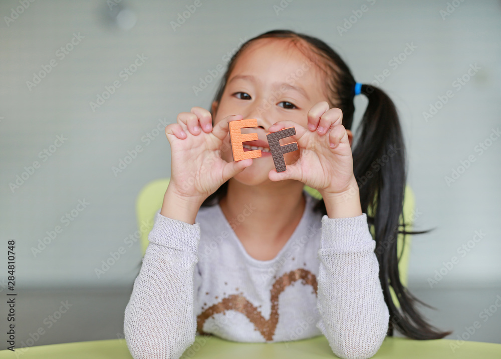 Happy little Asian child girl holding alphabet EF (Executive Functions) text on her face. Education and development concept. Happy little Asian child girl holding alphabet EF (Executive Functions) text on her face. Education and development concept.