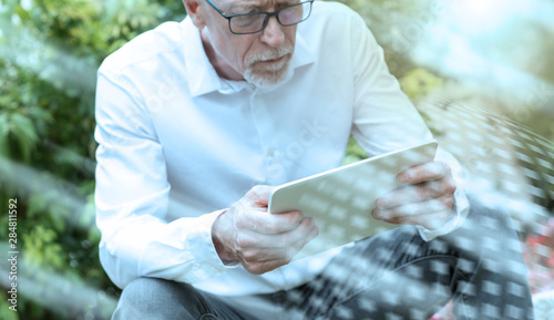 Mature man using his tablet outdoors, light effect; multiple exposure
