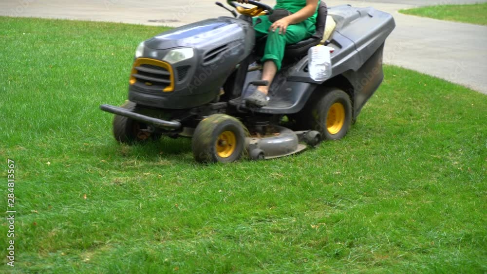 crop shot of workers riding on industrial lawn mowers and cutting grass in park