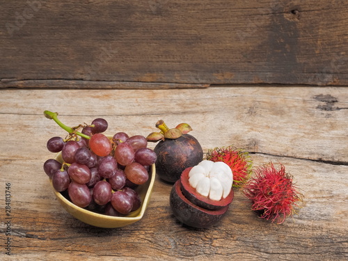 view of ripe grapes in a dish with ambutans and mangosteens three kind of Thai fruits on wood texture background.