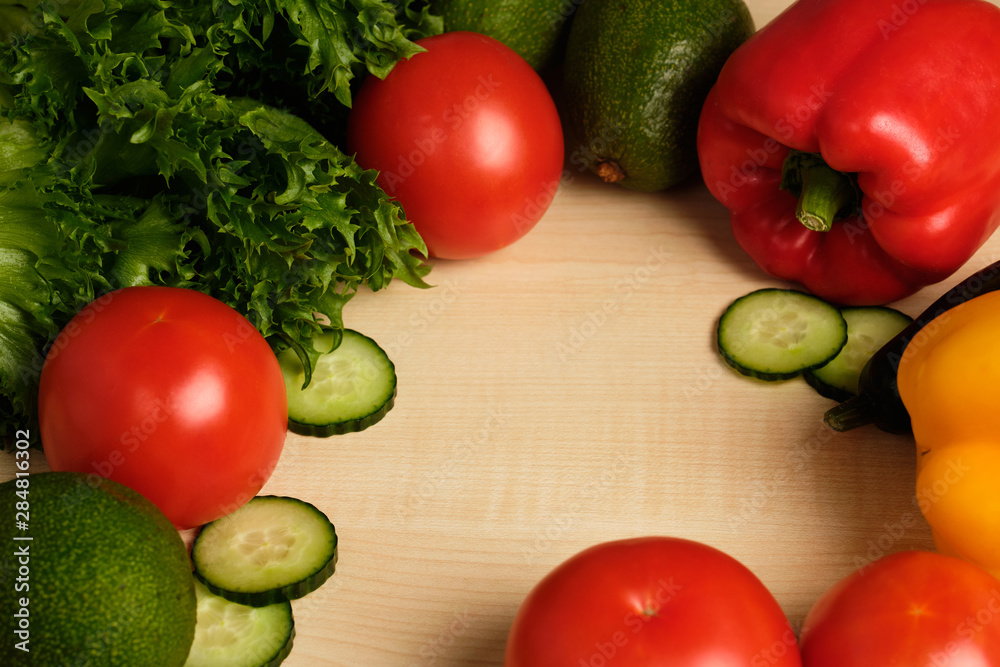 Vegetables are lying on a light wooden table with empty space in the middle. Vegetables are lying on a light wooden table with empty space in the middle.