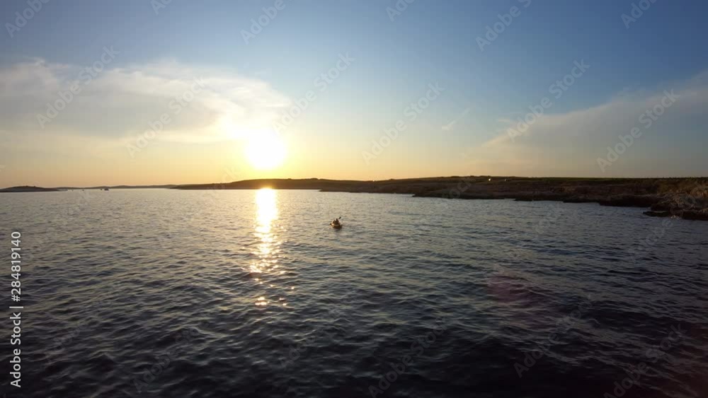 Aerial: Moving away from a person kayaking at sea at sunset Aerial: Moving away from a person kayaking at sea at sunset