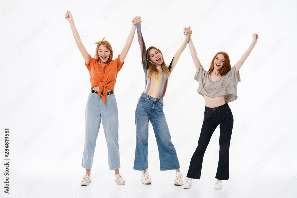 Portrait of three young girls wearing casual clothes smiling and raising arms together Portrait of three young girls wearing casual clothes smiling and raising arms together