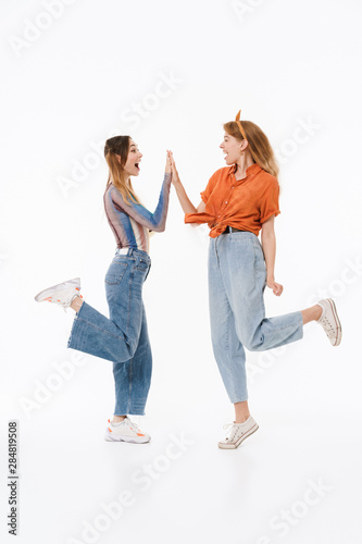Full length portrait of two positive girls wearing casual clothes smiling and giving high five together