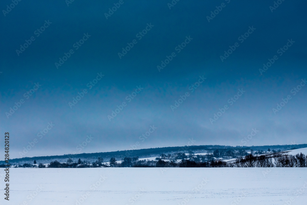 Winter landscape with snowy field and dark blue sky_