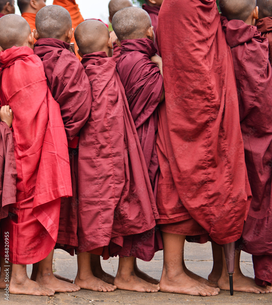 young buddhist pilgrims dressed in red traditional robes waiting to receive merit in myammar