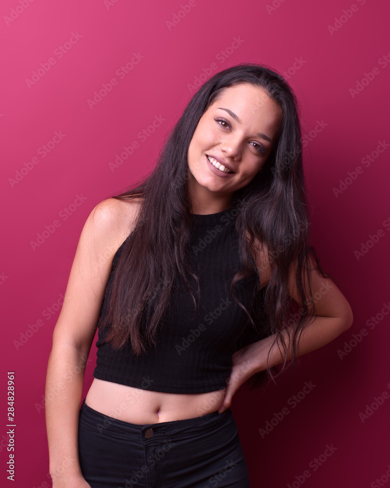 cheerful beautiful brunette girl in front of a red background poses with her hand on her hip while smiling and looks at the camera cheerful beautiful brunette girl in front of a red background poses with her hand on her hip while smiling and looks at the camera
