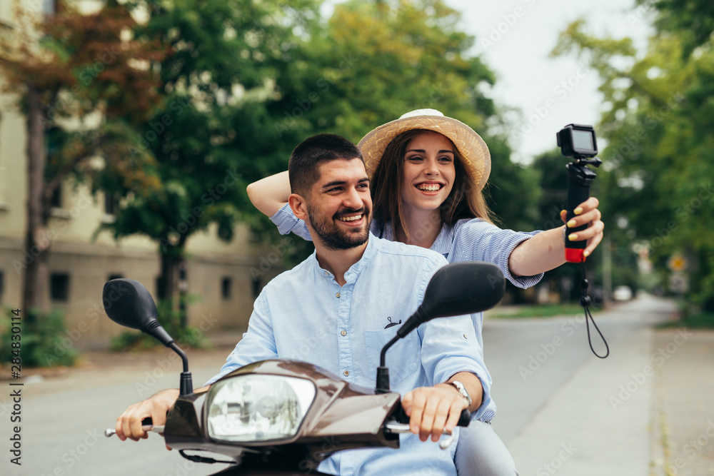 couple riding on a motorbike and taking picture with camera